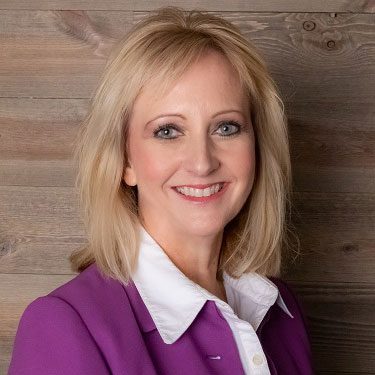 smiling woman standing in front of wood wall