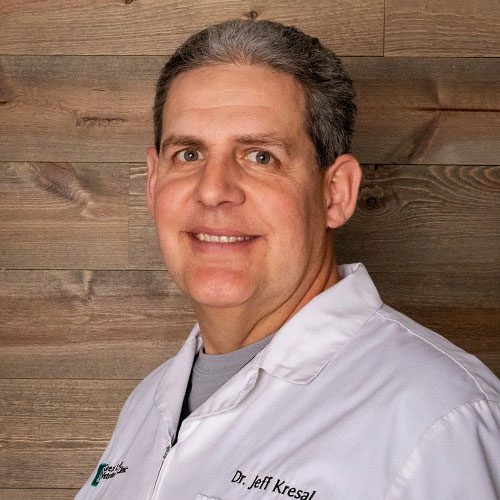 smiling male veterinarian standing in front of wood panel wall