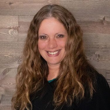 smiling woman standing in front of wood panel wall